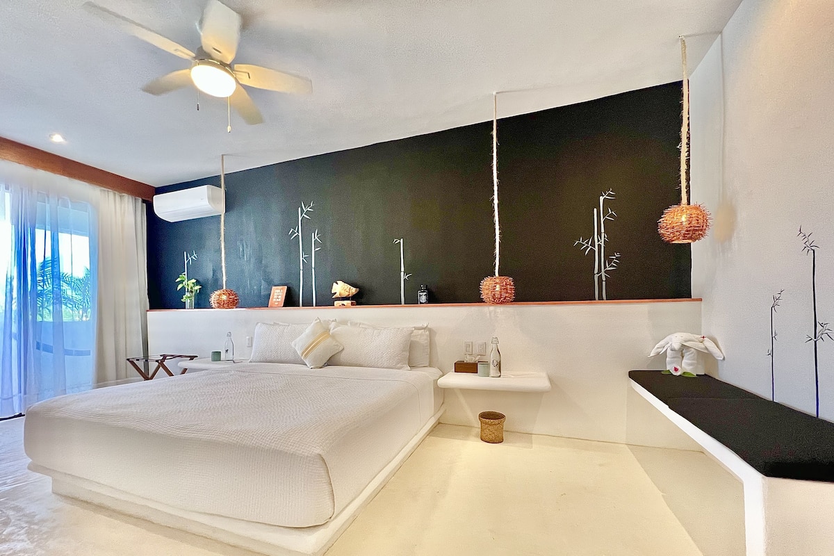 Un dormitorio moderno con una cama grande, un ventilador de techo, una mesita de noche y una ventana con cortinas.