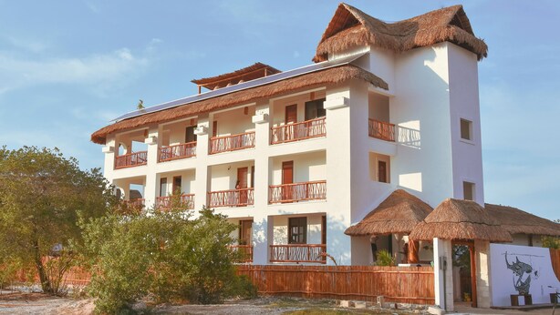 A multi-story hotel with thatched-roof balconies and a white facade. - Hotel Casa HX - Adults Only (Isla Holbox)