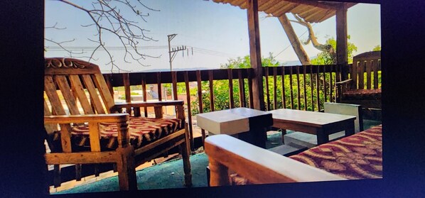 An outdoor seating area with wooden furniture and a view of greenery and a power line. - BEAUTYFUL, CASA DEL CAMPO  (Quezaltepeque)