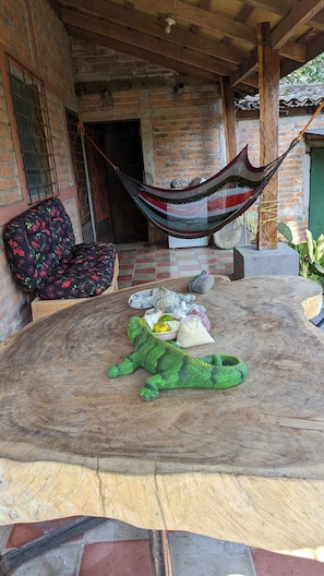 A hammock, a cushioned chair, and a round wooden table with various items on it. - BEAUTYFUL, CASA DEL CAMPO (Quezaltepeque)