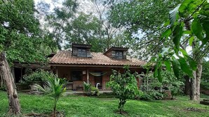 A rustic house with a tiled roof, surrounded by lush greenery and trees.