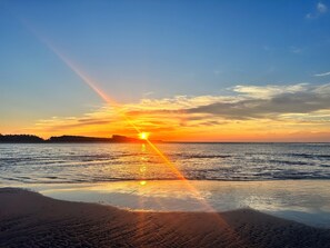 Ranta, josta avautuu näkymä auringonlaskuun meren yllä, tyyni vesi ja kirkas taivas.
