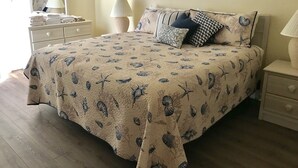 Un dormitorio con cama, mesitas de noche, lámpara, espejo y un cuadro en la pared.