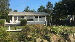 A single-story house with a front porch, a covered deck, and a small front yard with rocks and shrubs. - Waterfront - secluded beachfront 
Last Min Discount for week of August 29-Sept 5 (Portsmouth)