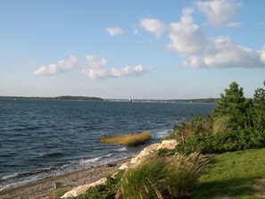 A coastal landscape with a rocky shoreline, a lighthouse in the distance, and a grassy area with vegetation. - Waterfront - secluded beachfront 
Last Min Discount for week of August 29-Sept 5 (Portsmouth)
