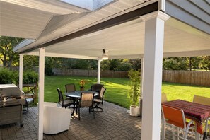 Une terrasse couverte équipée d’un barbecue, d’une table à manger, de chaises et d’une plante en pot.