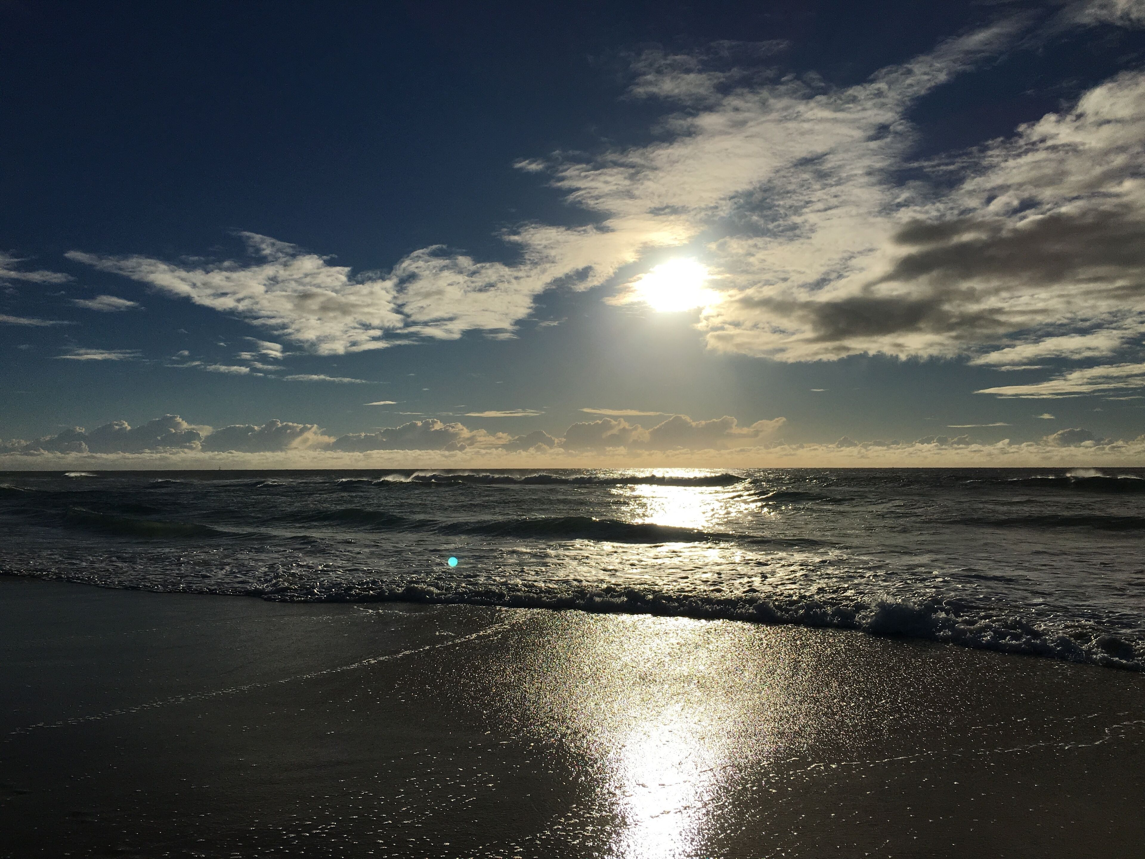 A beach with waves and a sun reflecting on the sand.
