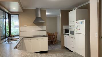 A modern kitchen with white cabinets, granite countertops, a stainless steel range hood, a double oven, and a refrigerator with magnets.