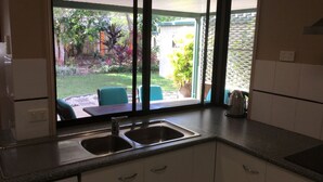 A kitchen with two sinks, a countertop, and a view of a garden with chairs and a table.