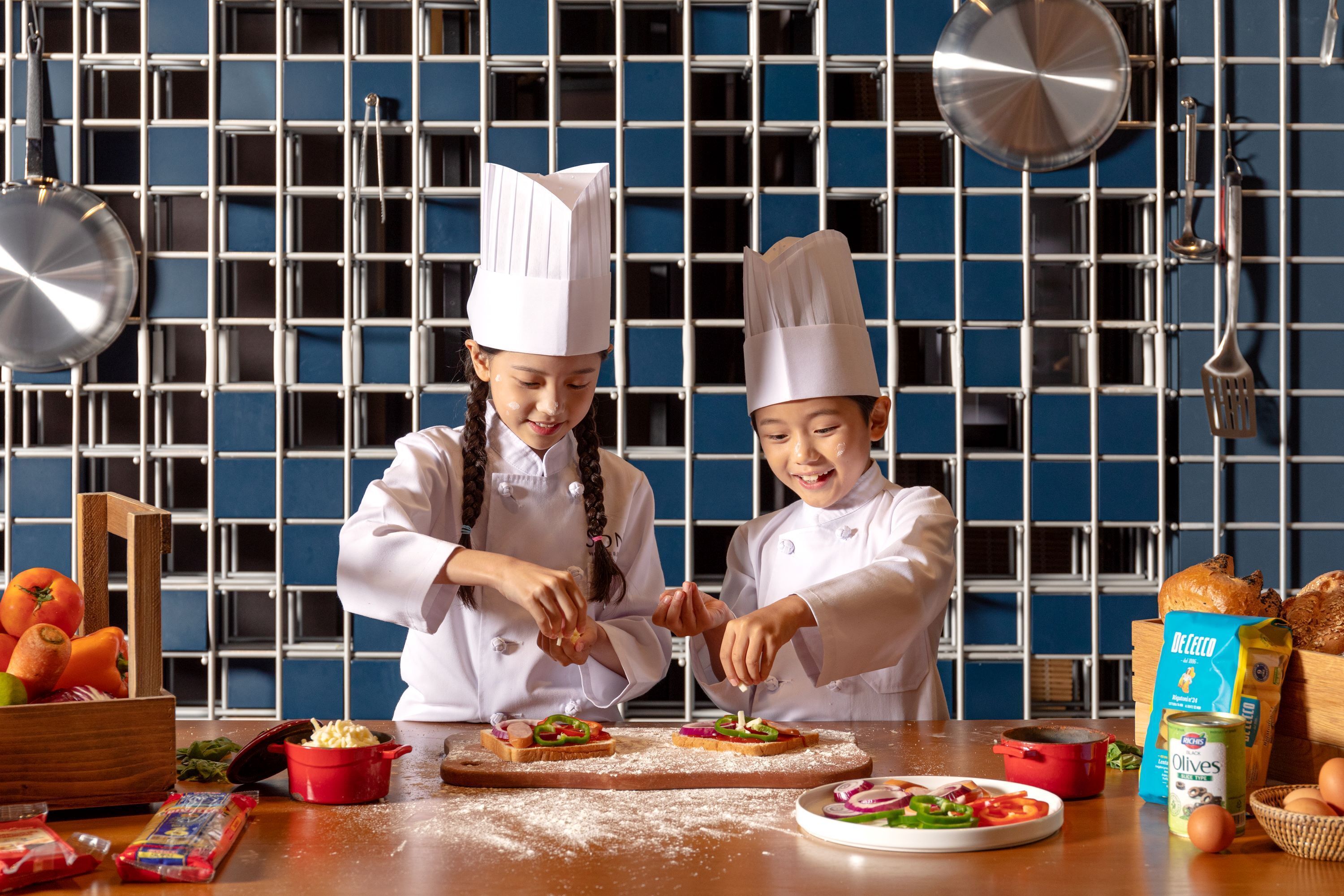 Two individuals in chef hats preparing food on a wooden board, with kitchen utensils and ingredients around them.