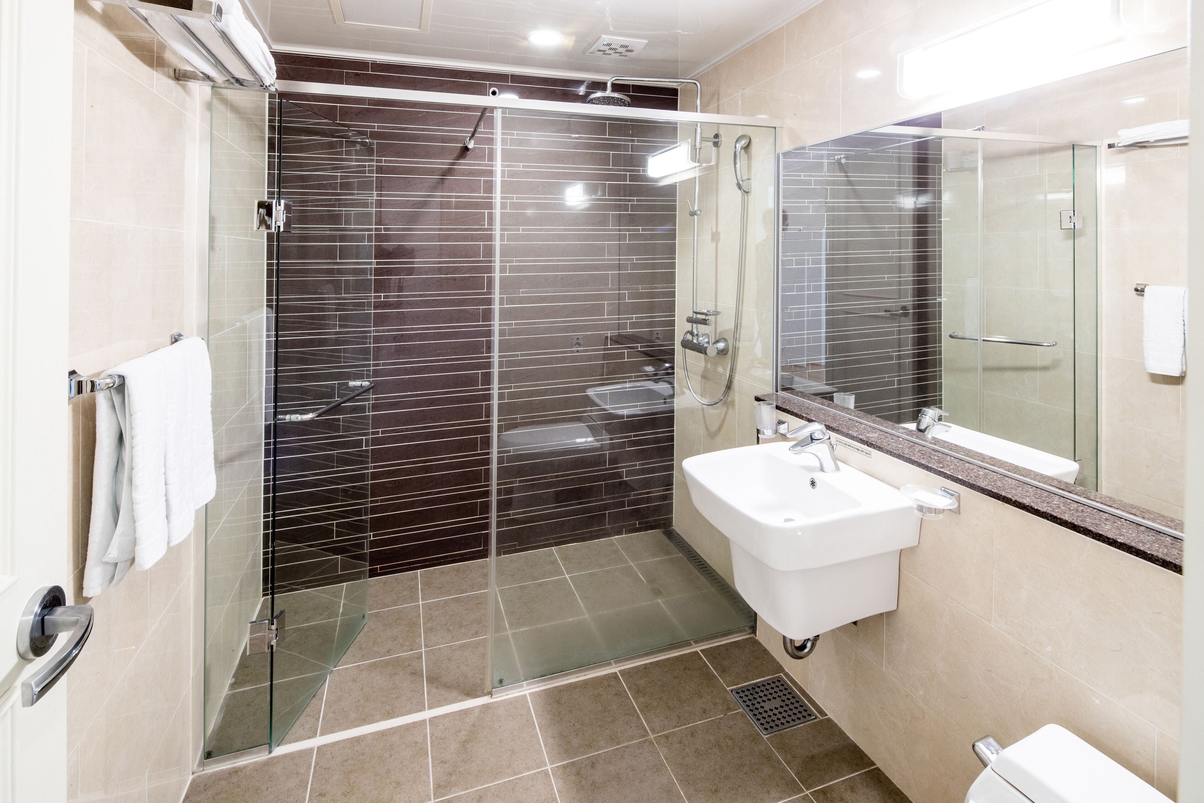 A modern bathroom with a glass-enclosed shower, a white sink, and a large mirror.