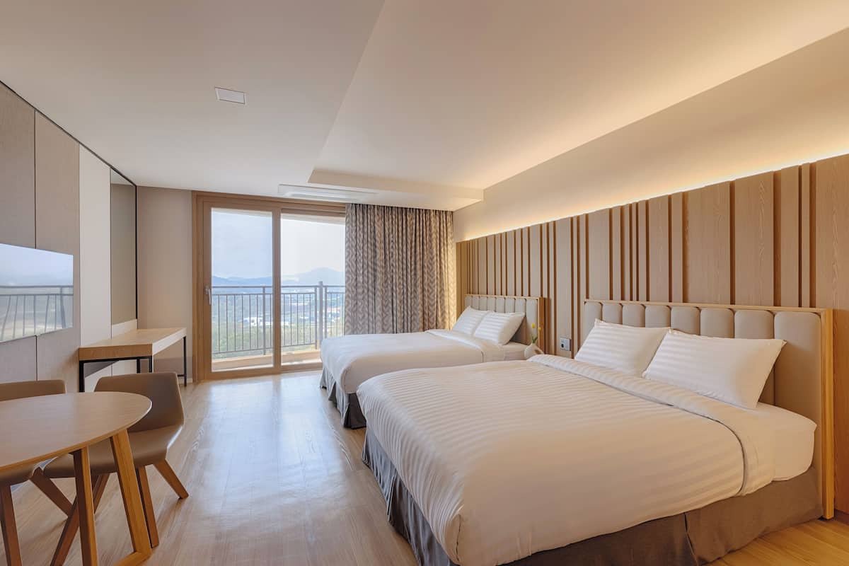 A modern hotel room with two beds, a desk, and a balcony with a view.