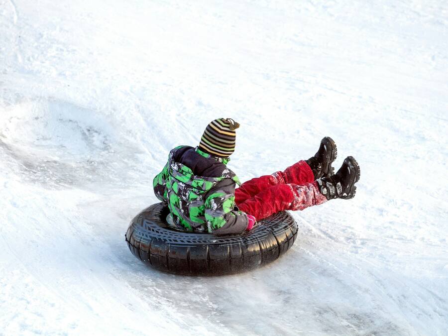 A person sledding down a snowy slope on a large tire.