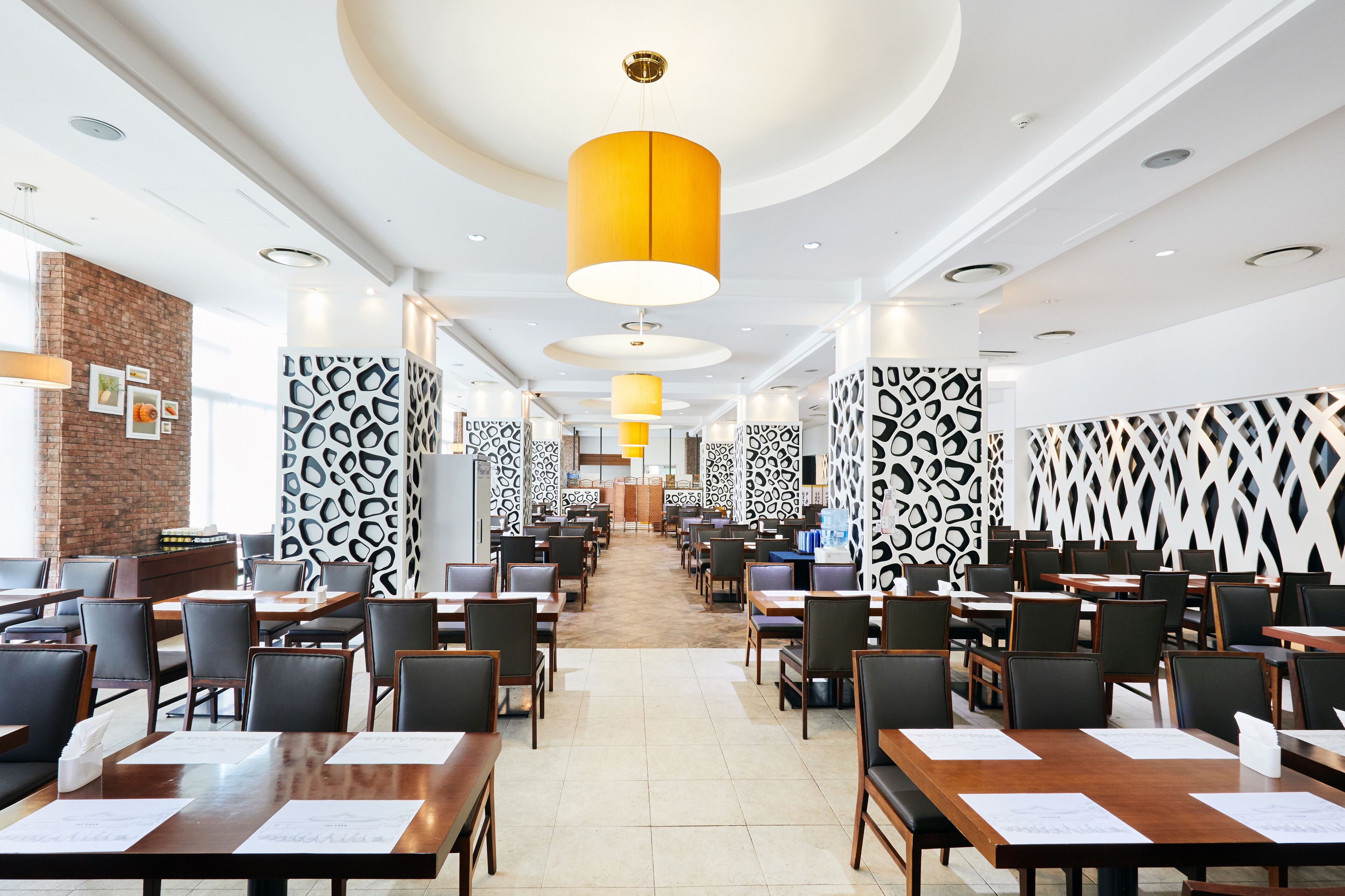 A spacious restaurant with high ceilings, modern pendant lighting, and a central walkway.