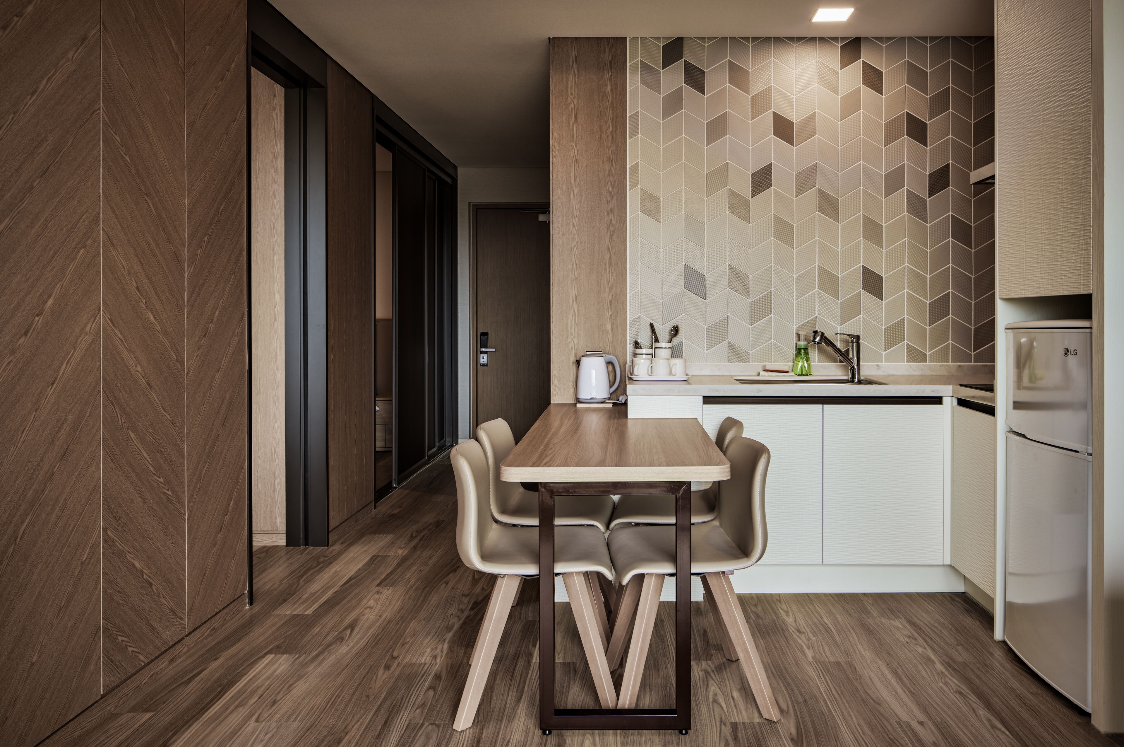 A modern kitchen with a wooden dining table, chairs, a coffee maker, and a refrigerator.