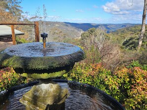 A stone fountain with water spouting from the top, surrounded by lush greenery and a view of distant hills. - STUNNING VIEWS, 6 bedrooms, 12 people, fireplace, early check-in, late check-out (Mount Victoria)