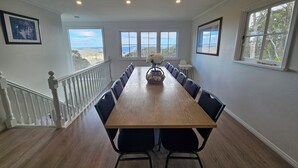 A dining room with a long wooden table, black chairs, and a view of the outdoors. - STUNNING VIEWS, 6 bedrooms, 12 people, fireplace, early check-in, late check-out (Mount Victoria)