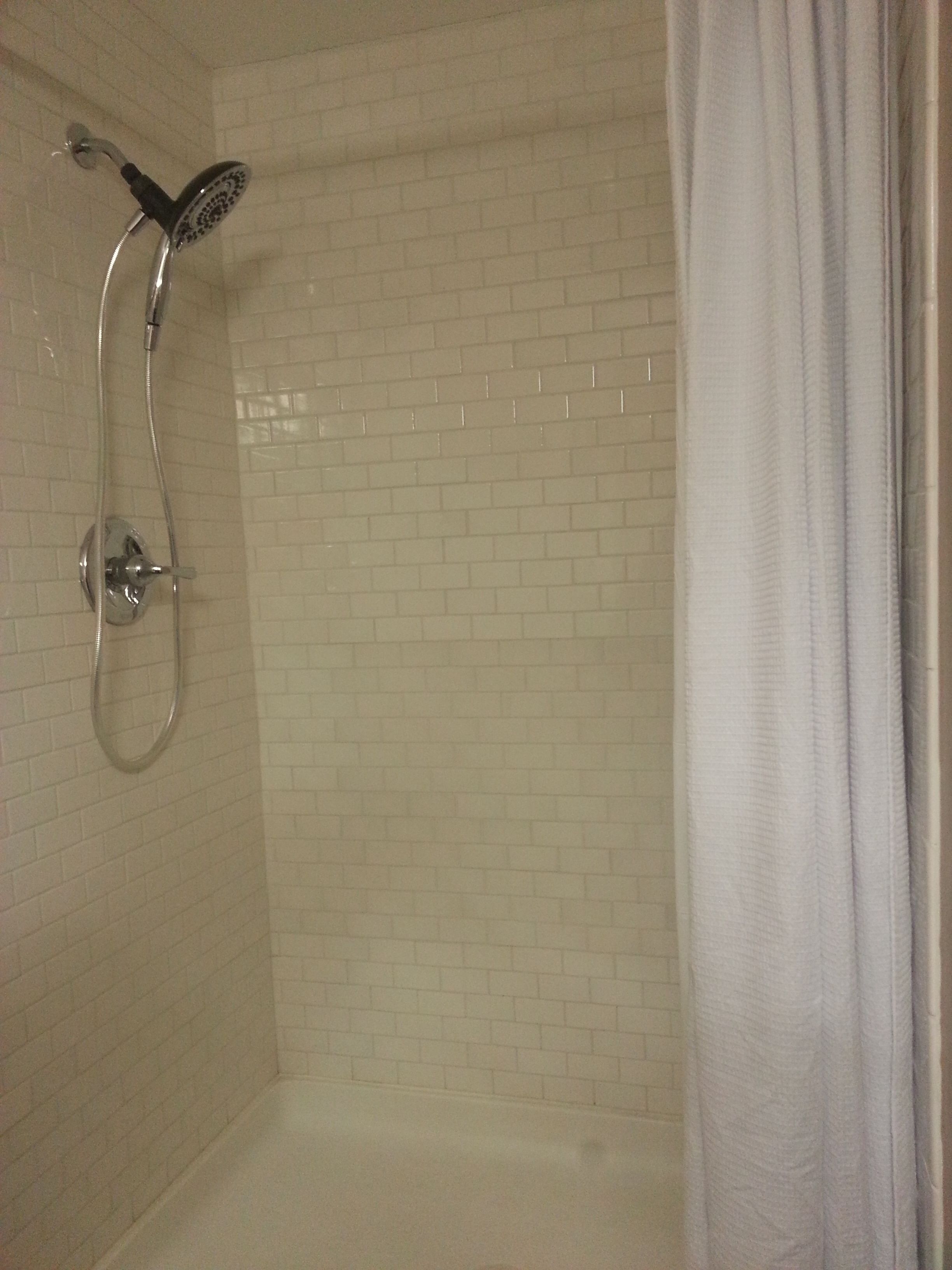 A shower with a handheld showerhead and a wall-mounted faucet.
