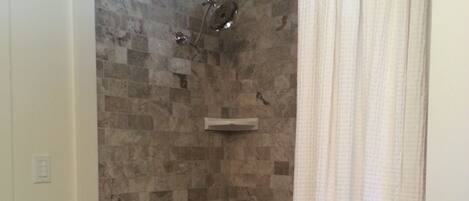Un baño con pared de ducha de mosaico de piedra, una bañera y una cortina de ducha blanca.