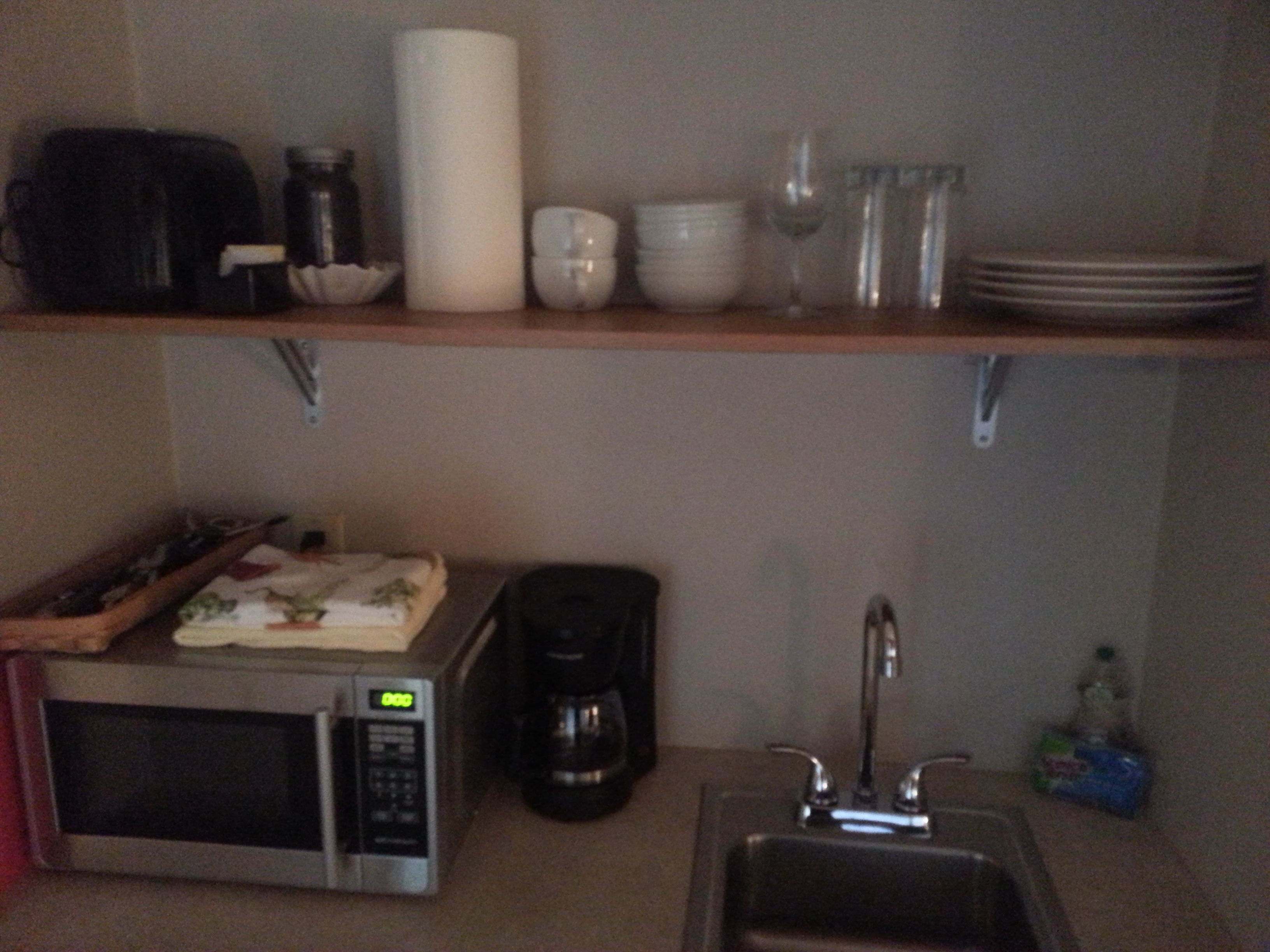 Una cocina equipada con microondas, cafetera, pileta y diferentes vajillas en los estantes.