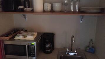 Una cocina equipada con microondas, cafetera, pileta y diferentes vajillas en los estantes.