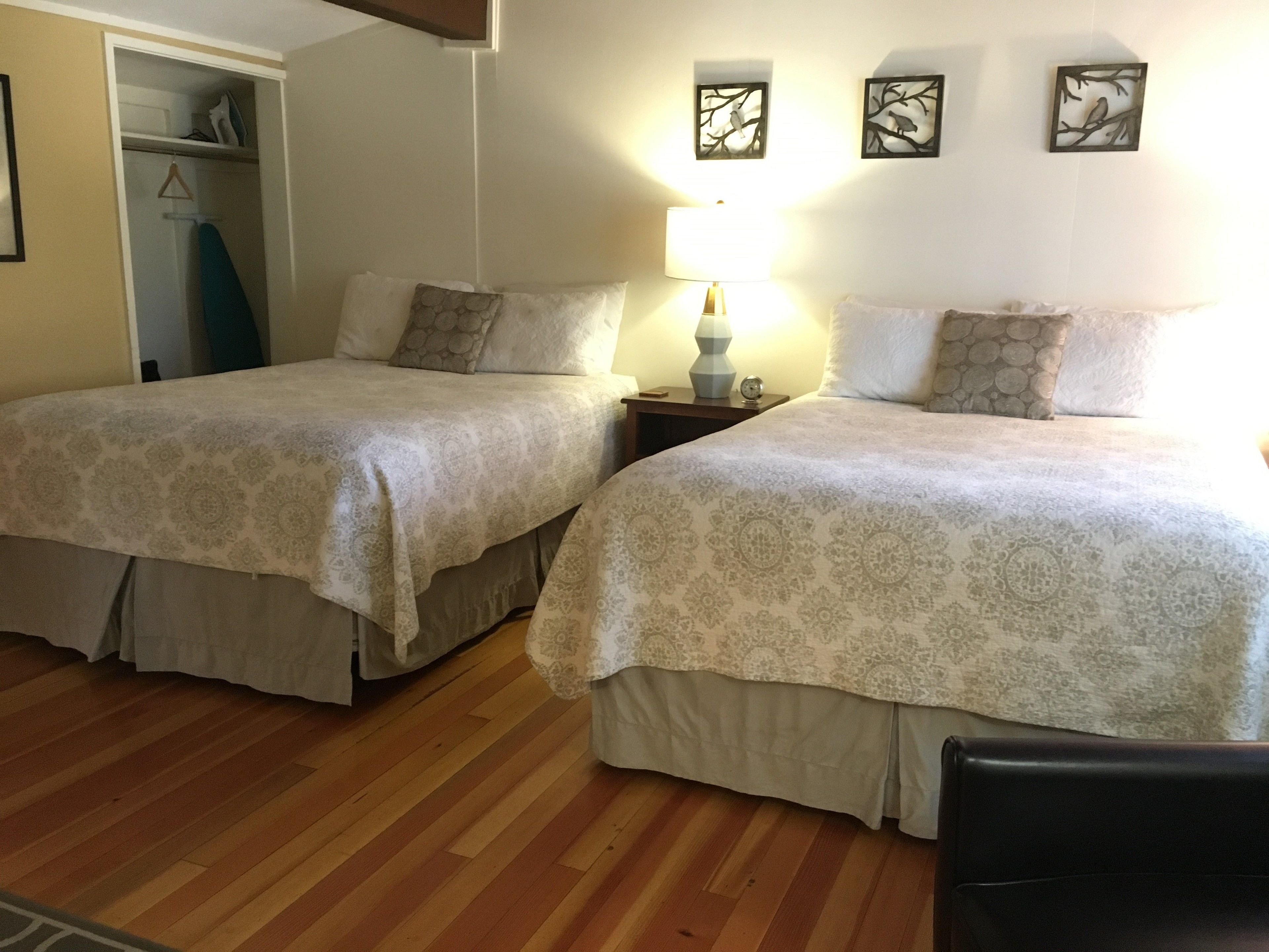 A room with two beds, a wooden floor, a closet, and wall art.