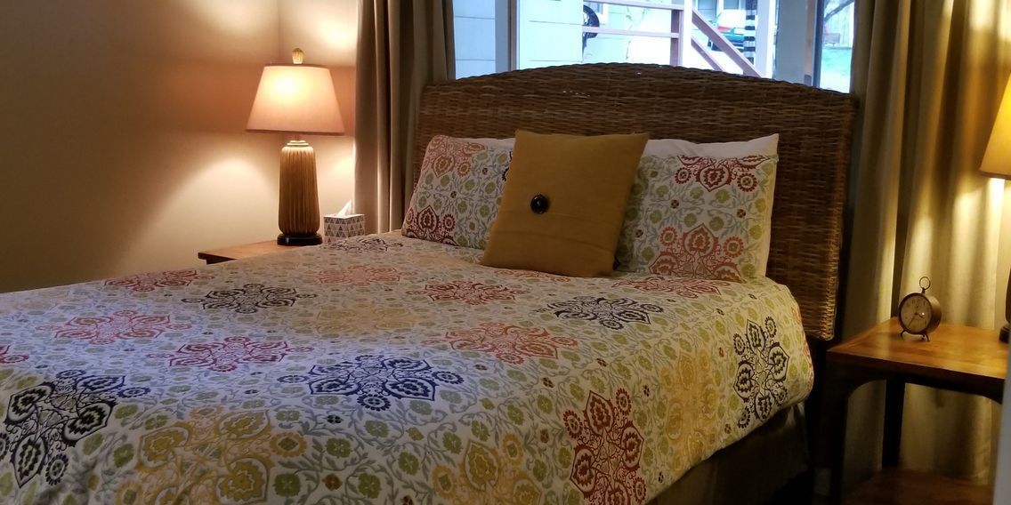 Un letto rifatto con cura, una comodino con una lampada e vista su un edificio.