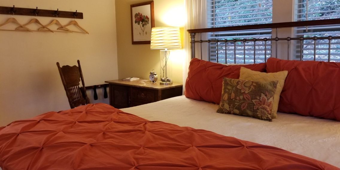 Ein Schlafzimmer mit einem Bett, einem Nachttisch, einer Lampe, einem Sessel und einem Fenster mit Jalousien.