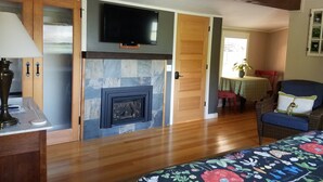 A room with a fireplace, wooden flooring, a television mounted above it, and a bed with a floral bedspread. - China Creek Cottages (Willow Creek)