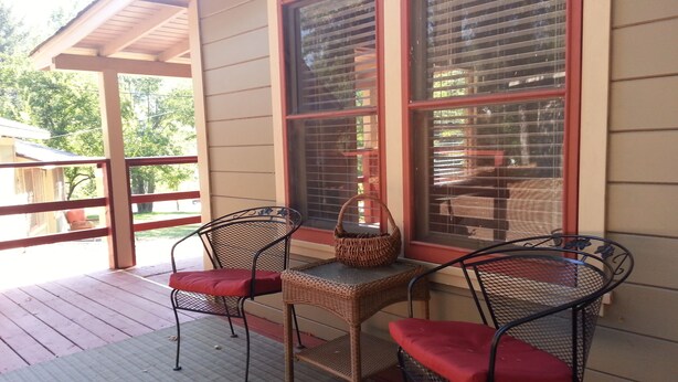 A covered porch with two wicker chairs and a small table, featuring a basket on the table. - China Creek Cottages (Willow Creek)