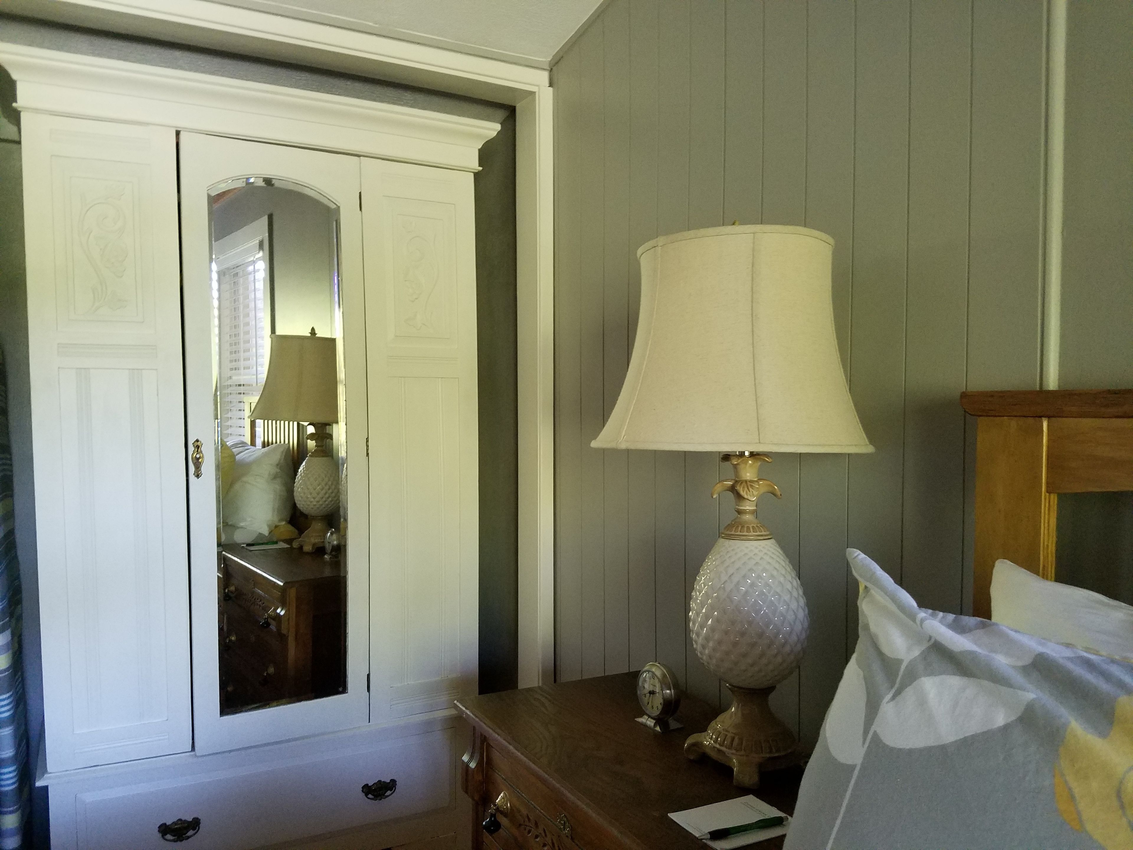 Um quarto com cômoda de madeira, luminária, espelho e guarda-roupa.