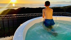 Una persona en un jacuzzi con vista a la puesta de sol sobre el océano.