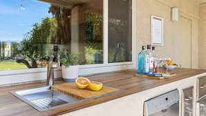 A kitchen with a built-in dishwasher, a wooden countertop, a sink, and a window overlooking a garden. - Private Pool Resort Home - Walk to Music Festivals Polo Grounds (Indio)