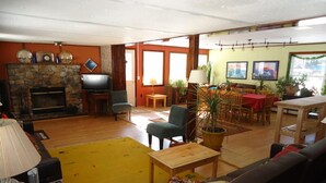 Ein geräumiges Wohnzimmer mit Kamin aus Stein, einem Fernseher, einem Essbereich mit Tisch und Stühlen und einem gelben Teppich.