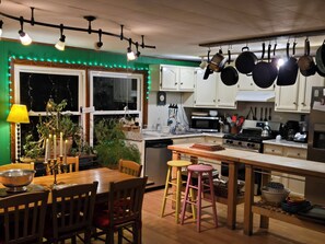 Een keuken met hangende pannen, een eettafel met stoelen, een fornuis en een raam met lichtjes.