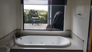 Une salle de bain avec une baignoire, une fenêtre donnant sur un balcon et offrant une vue sur le paysage extérieur.