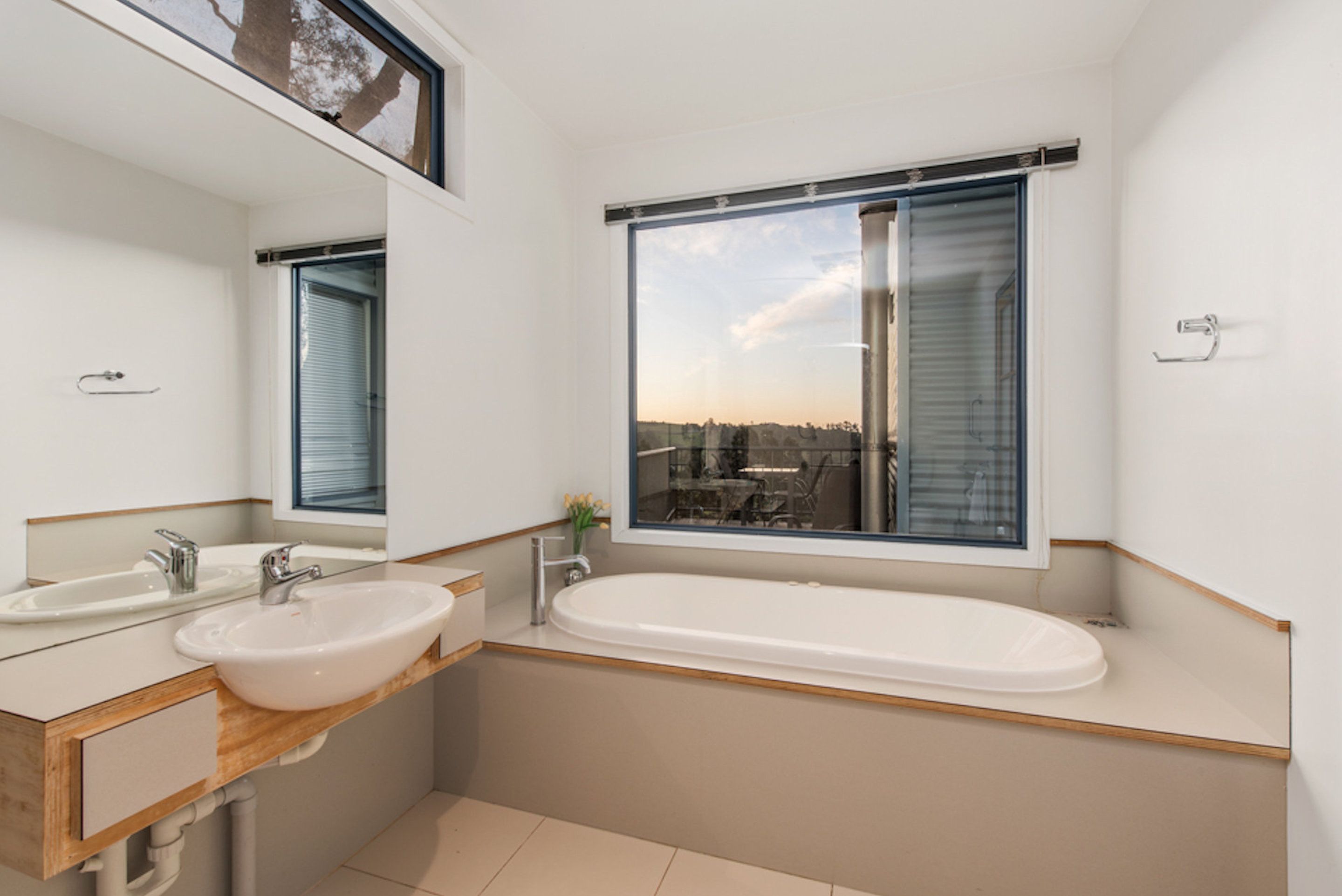 A modern bathroom with a large window, a bathtub, and a double sink.
