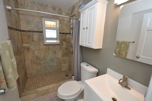 A bathroom with a shower, toilet, sink, and a window.