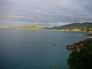 A coastal landscape with calm waters, green hills, and scattered buildings.