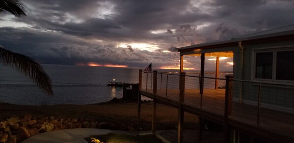A coastal view with a wooden deck overlooking the sea, a dock, and a building with an American flag.