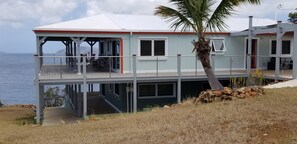 A coastal house with a balcony, a view of the sea, and a palm tree.