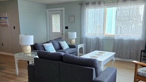 A living room with a grey sofa, two side tables with lamps, a white coffee table, and a window with sheer curtains. - 3 bedroom 2 bathroom, pet friendly, ocean front duplex (Emerald Isle)