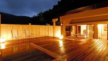 An outdoor wooden deck with chairs and a table, surrounded by a wooden fence and a building with glass doors.