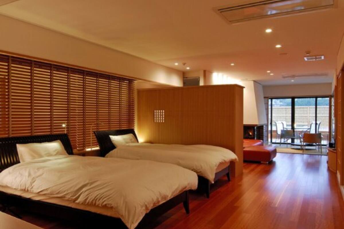 Habitación de hotel con dos camas, persianas de madera, un sofá y vista a la ciudad.