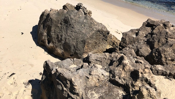 Une plage avec de gros rochers au premier plan et un ciel bleu dégagé.