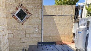 Un espace patio avec une table et des chaises en métal, une petite fenêtre et un climatiseur fixé au mur.