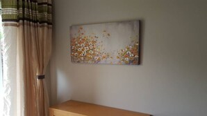 Une pièce avec une table en bois, des rideaux de couleur beige et un tableau floral accroché au mur.