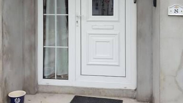 Une porte blanche avec un panneau de verre, une petite marche menant à la porte, et une plaque numérotée « 8 » sur le mur.