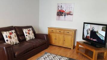 Een woonkamer met een bruine leren bank, een houten kast, een televisie op een houten dressoir en een kamerbreed tapijt met een patroon.