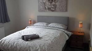 Une chambre à coucher avec un grand lit, deux tables de chevet avec des lampes, une tête de lit et une œuvre d’art accrochée au mur.